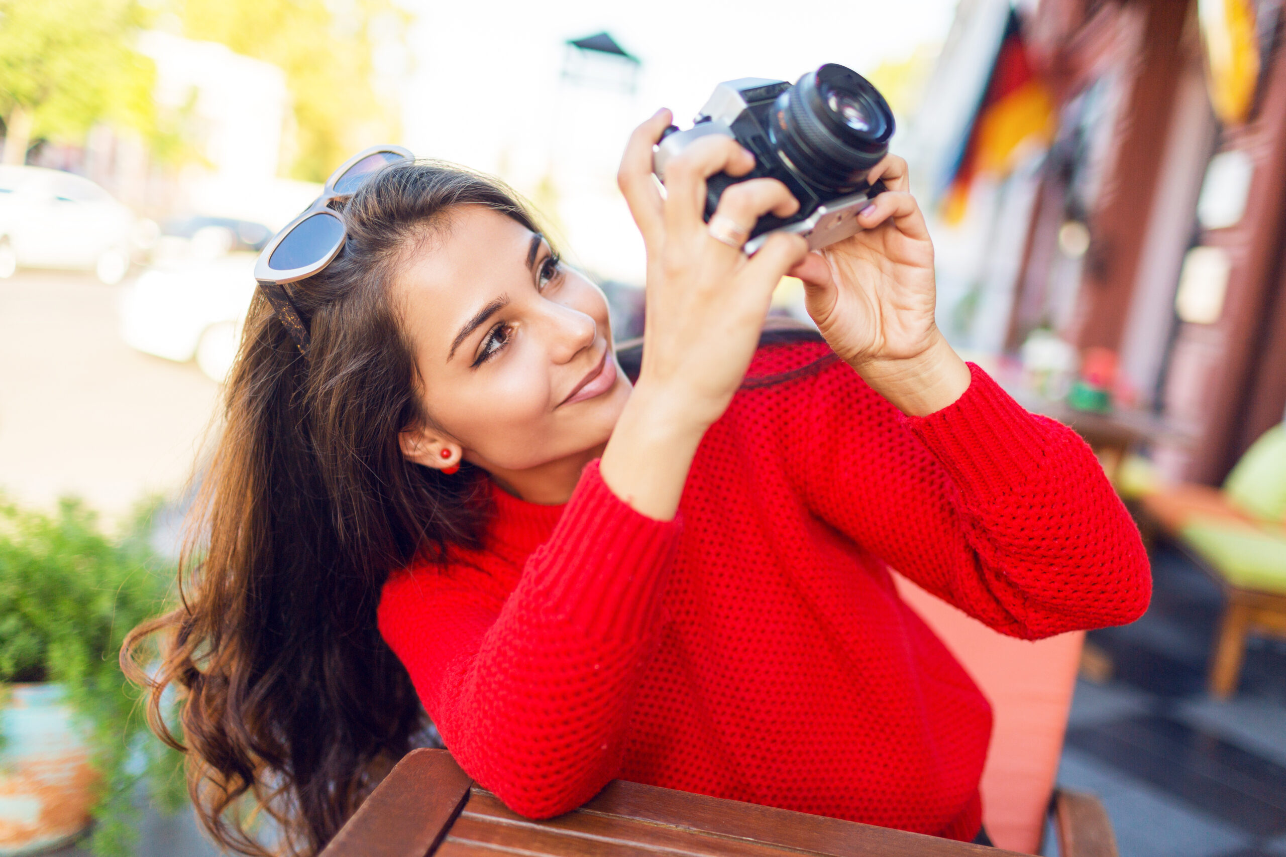Enthusiastic  long hairs woman looking up, making picture, enjoying amazing architecture in old European city.  Spring or fall season. Cozy knitted red sweater. Sunny weather. Warm colors.